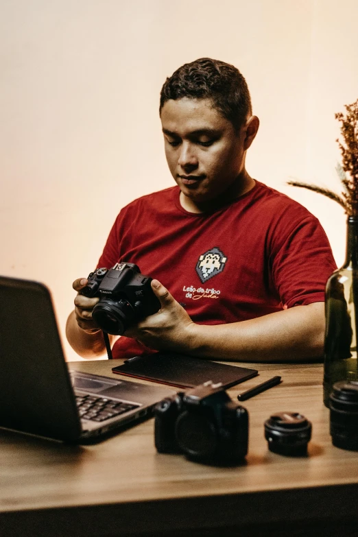 man in a red shirt using his camera next to a laptop computer