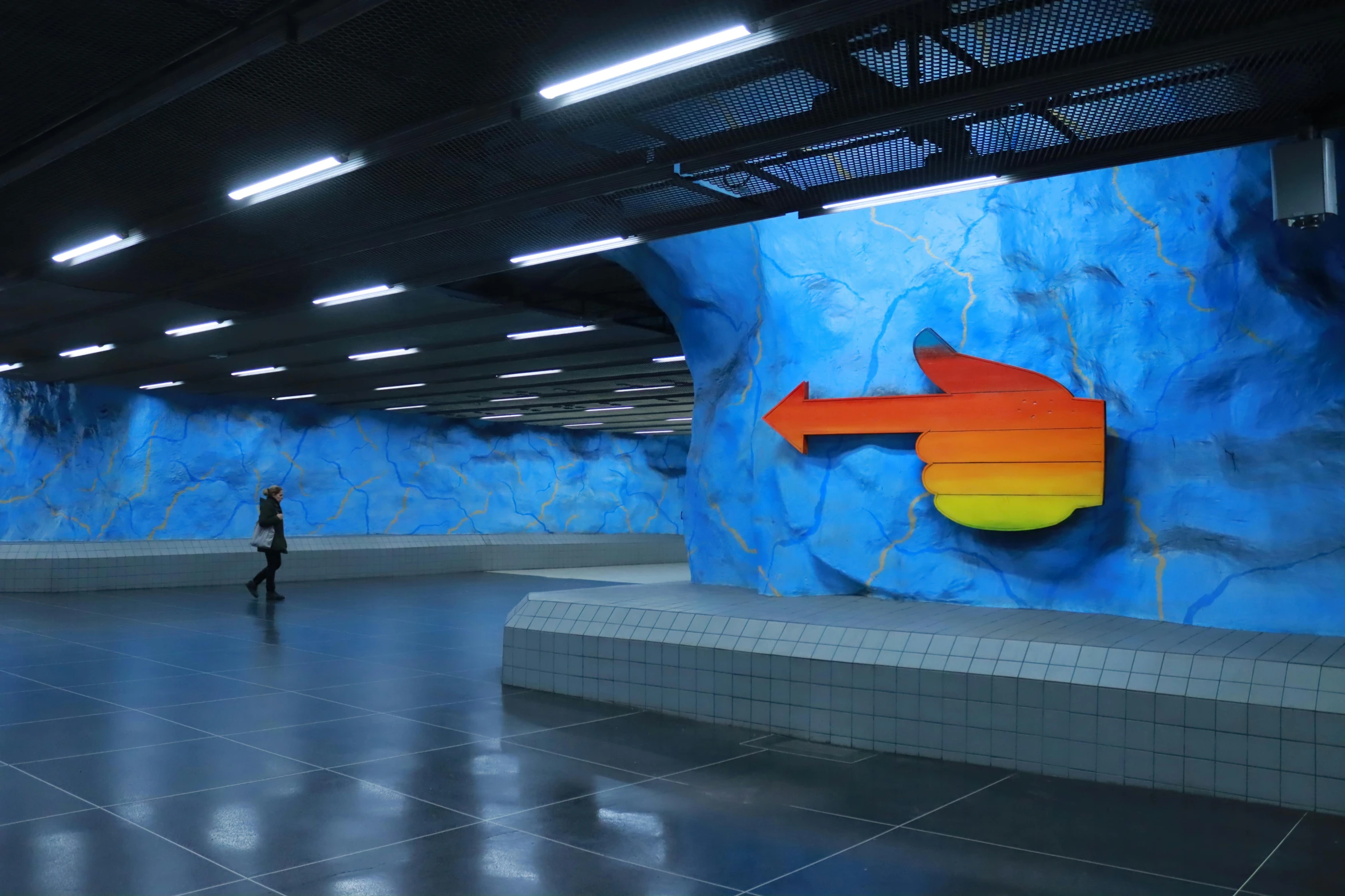 a person standing next to a blue mural of a colorful arrow