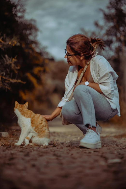 woman pets an orange tabby cat in a field