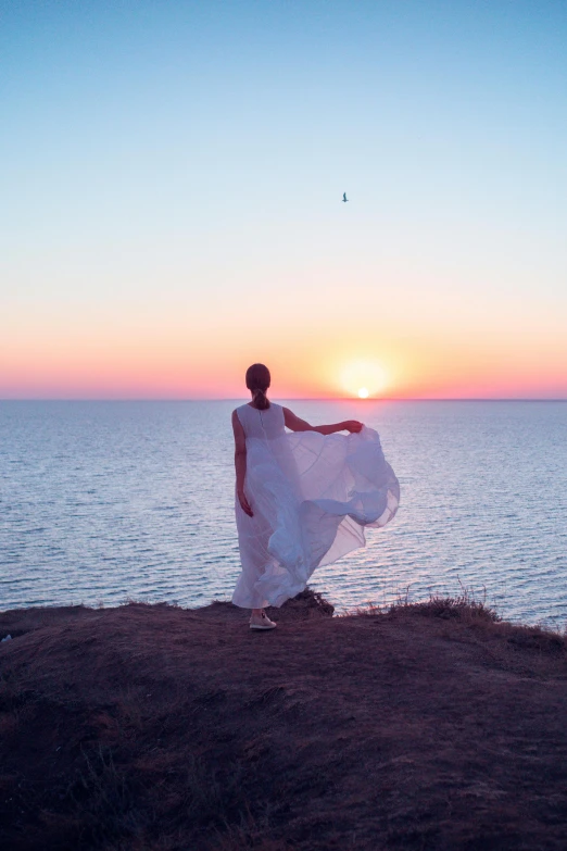 woman in flowing dress standing on shore overlooking ocean