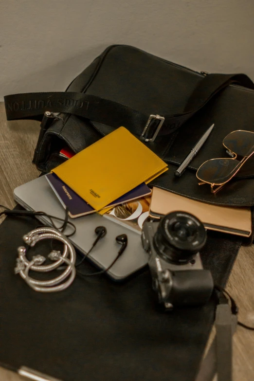 a small camera sitting next to a books, sunglasses, a pen and a notebook on a bed