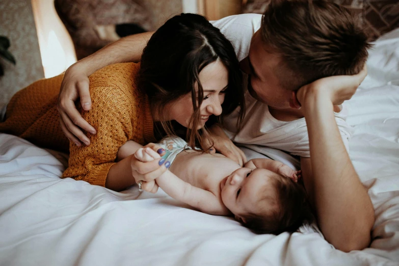 a woman and a man are looking at a baby while they lie on a bed