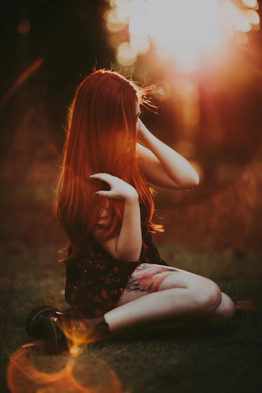 a beautiful redhead with a tattoo sitting in the grass