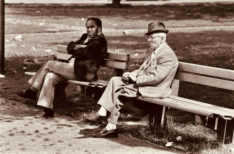 two older gentlemen sit on an old bench in the park