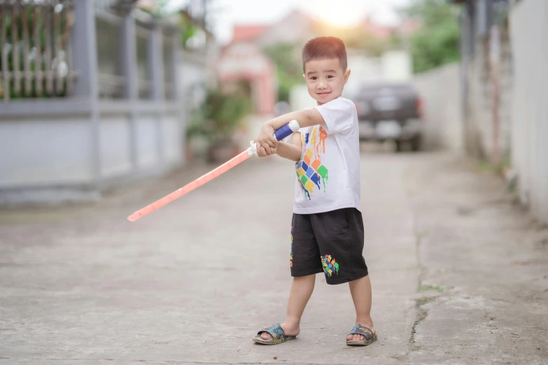 boy on a sidewalk holding onto a pink plastic bat