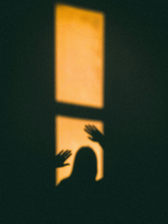 the silhouette of a person making gestures with their hands and holding up a window