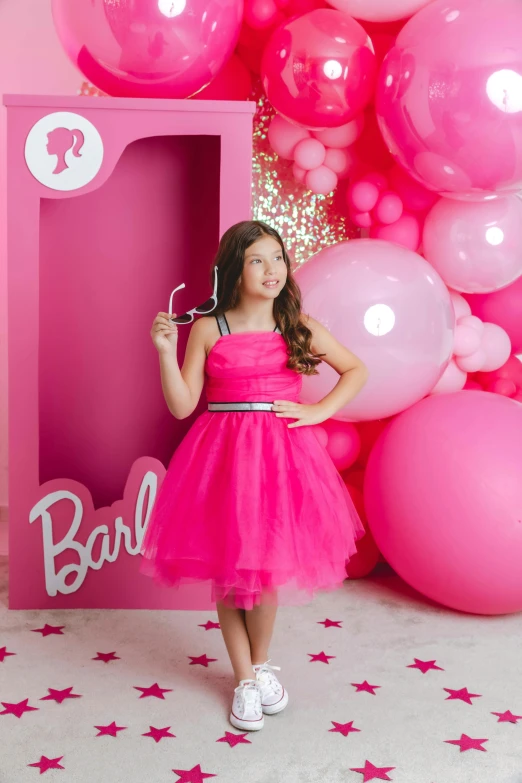 a pretty little girl wearing a pink dress with balloons around her
