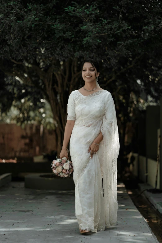 woman walking in a white saree and holding a bouquet