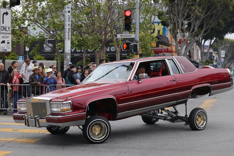 a red car drives down a street with people watching