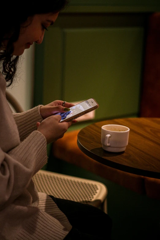 a woman uses her cell phone at a table with a mug