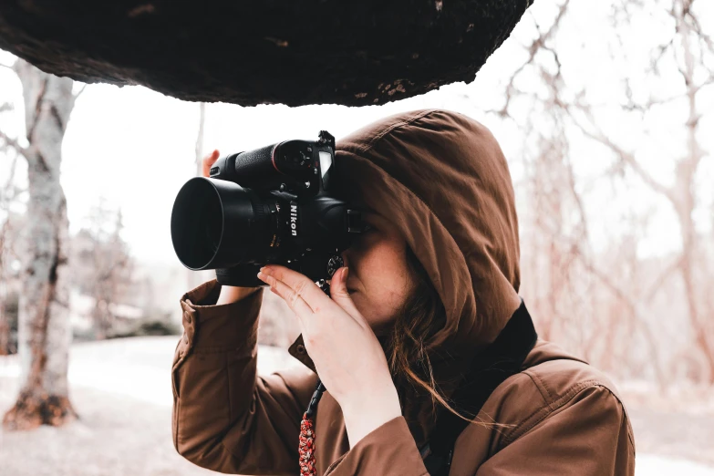 a girl wearing a brown hoody and holding up a digital camera