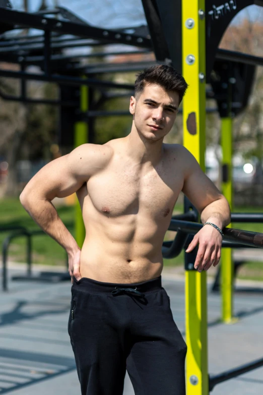 a shirtless young man leaning on a rack in the park