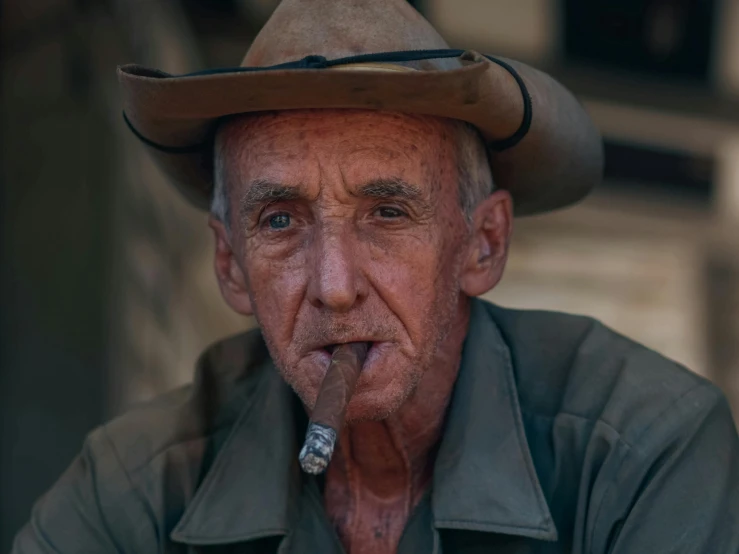 an old man with a cowboy hat holding a cigarette