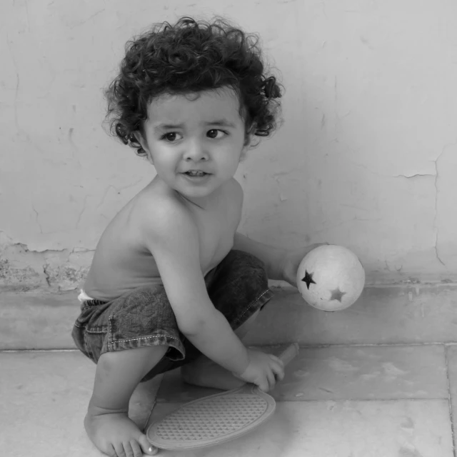 a young child holding a tennis ball sitting on the ground