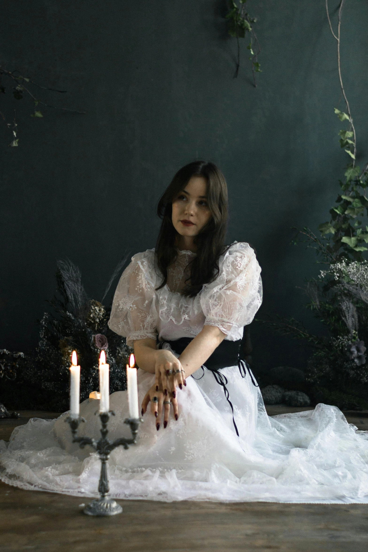 a girl sitting on the ground with candles and greenery