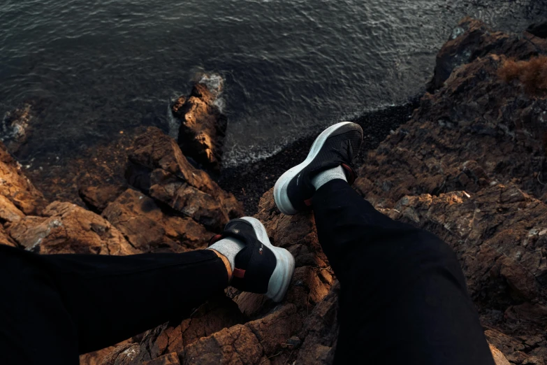 two people standing on some rocks next to a body of water