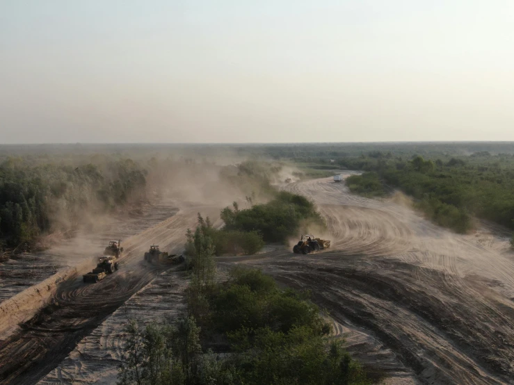 several trucks are driving on dirt road in open area