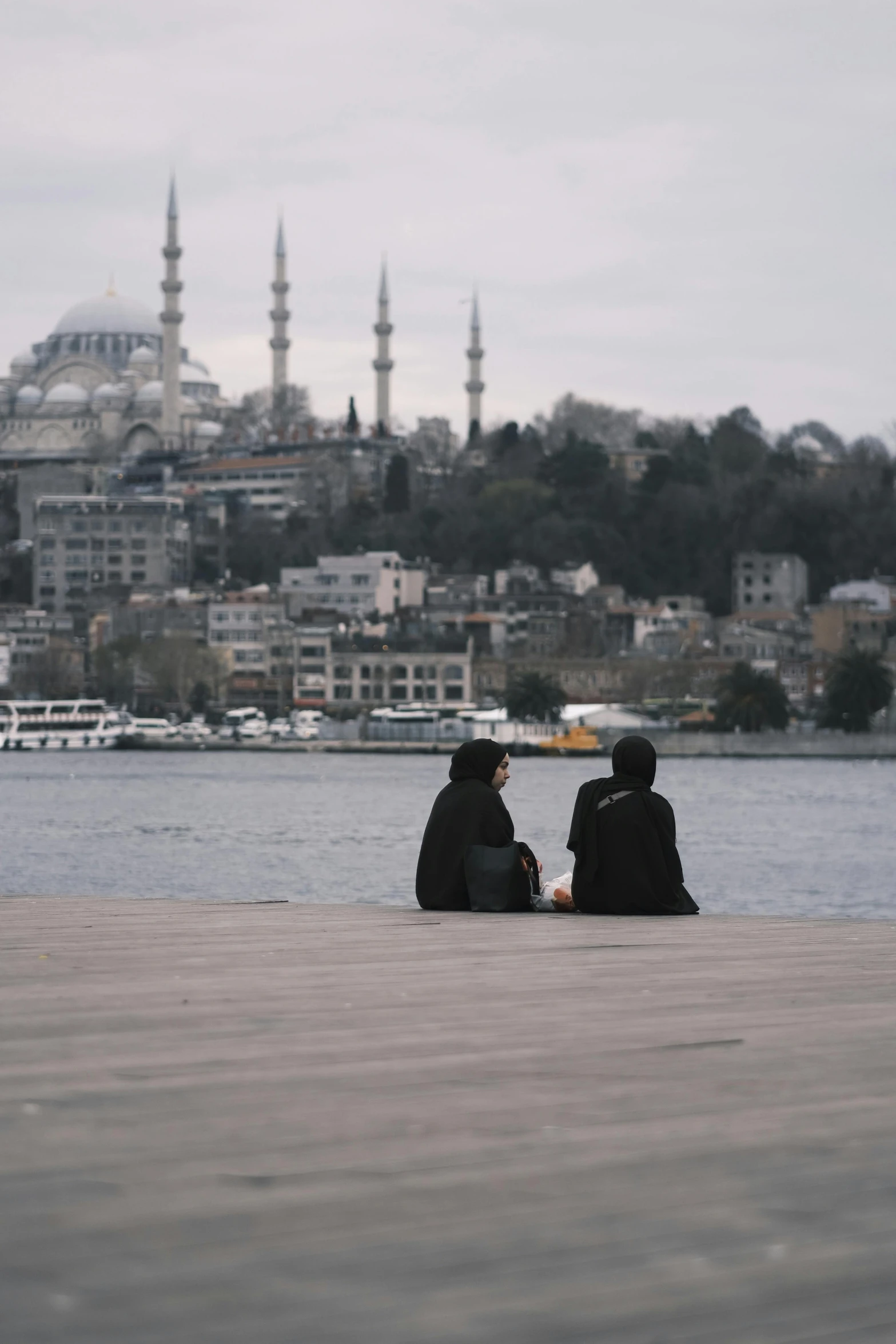 two people sit together on the ground by water