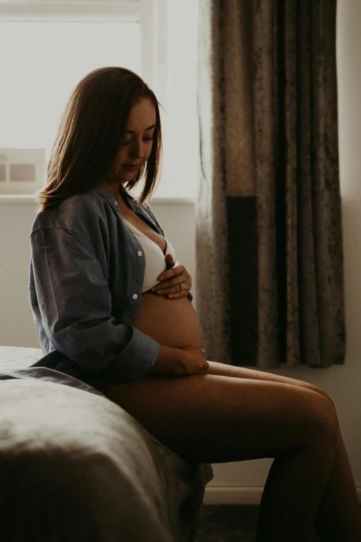 a pregnant woman sitting on a bed in her underwear