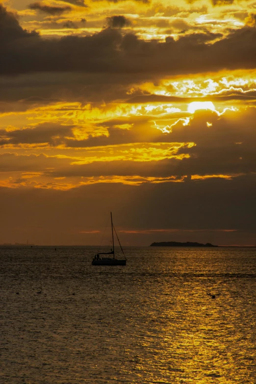 sunset at sea with sail boat floating through calm ocean