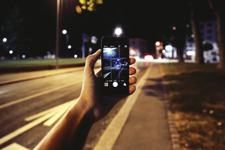 a person is holding up a cell phone with street lights in the background