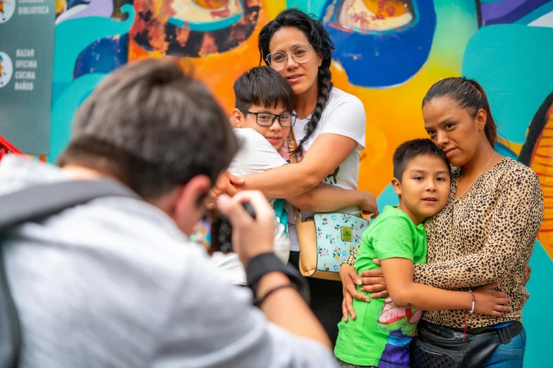 two adults and three children stand in front of a mural with a phone up to their ear