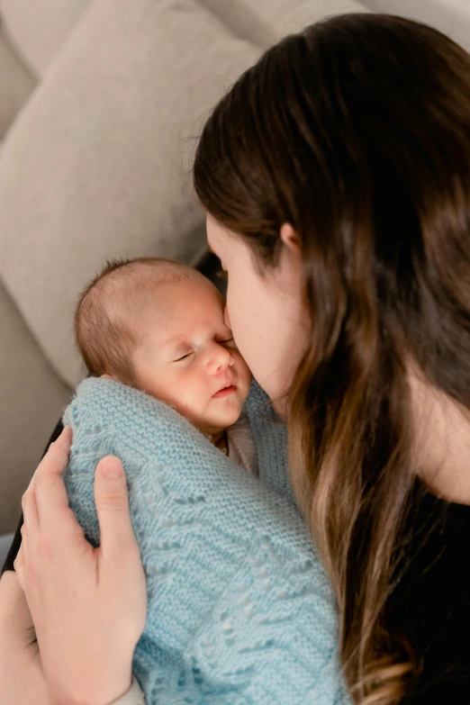 a woman in a blue sweater holds a sleeping baby