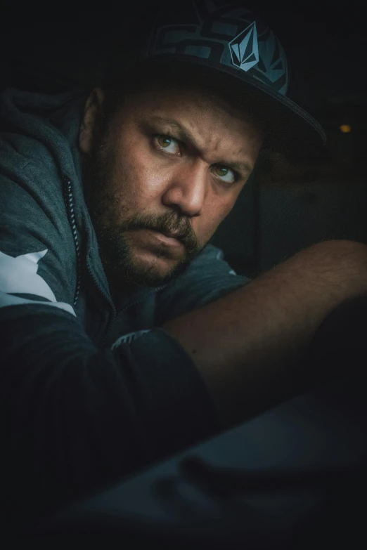 a man wearing a baseball cap and jacket leaning up against a wall