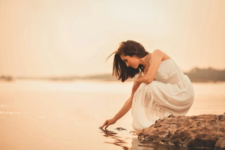 the girl is reaching into the water with a small object in her hand