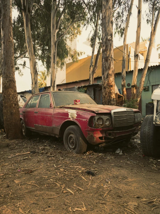 an old red truck is sitting next to a car in the forest