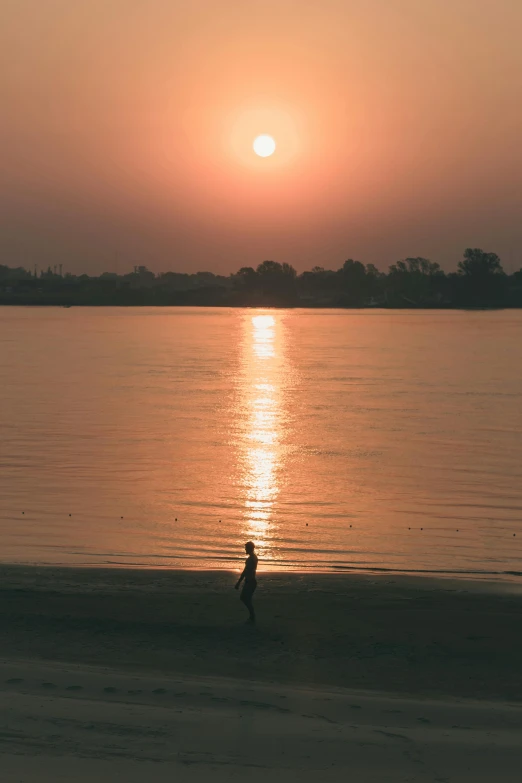 a person walking along the edge of a river while the sun sets