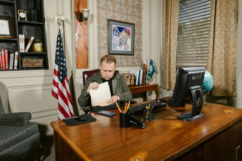 a man with an open notebook looks at a notepad as he works on a computer