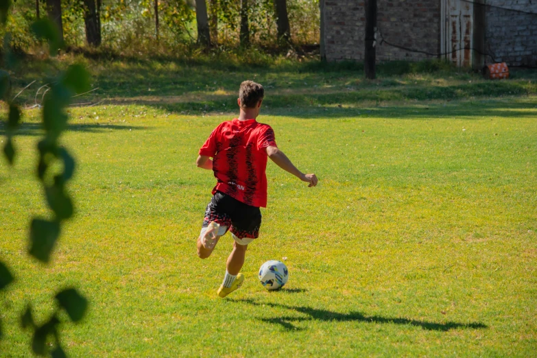 a boy in red jersey kicking soccer ball