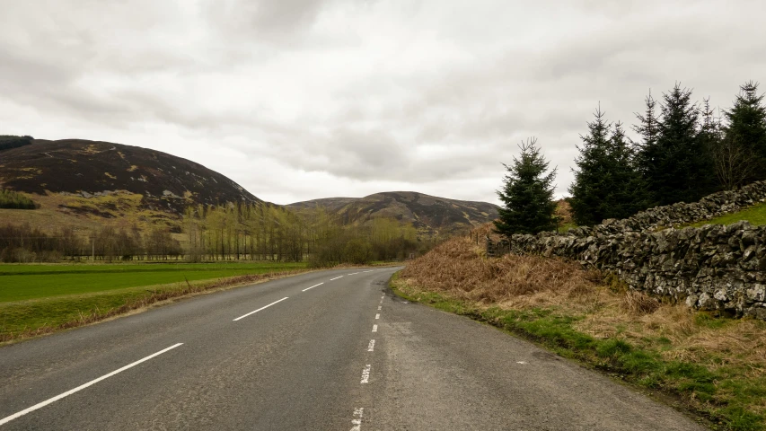 an empty paved road next to grassy fields