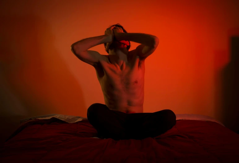 man sitting on red bed in bedroom with red wall and orange background