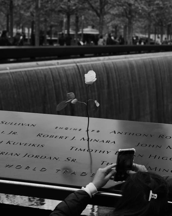 black and white pograph of a person using a phone near a memorial