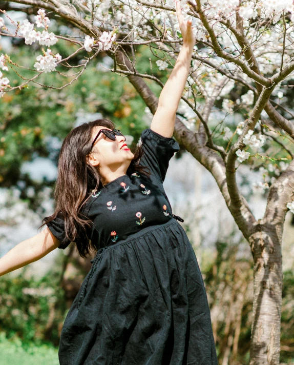 a woman wearing sunglasses reaches up for a cherry blossom tree