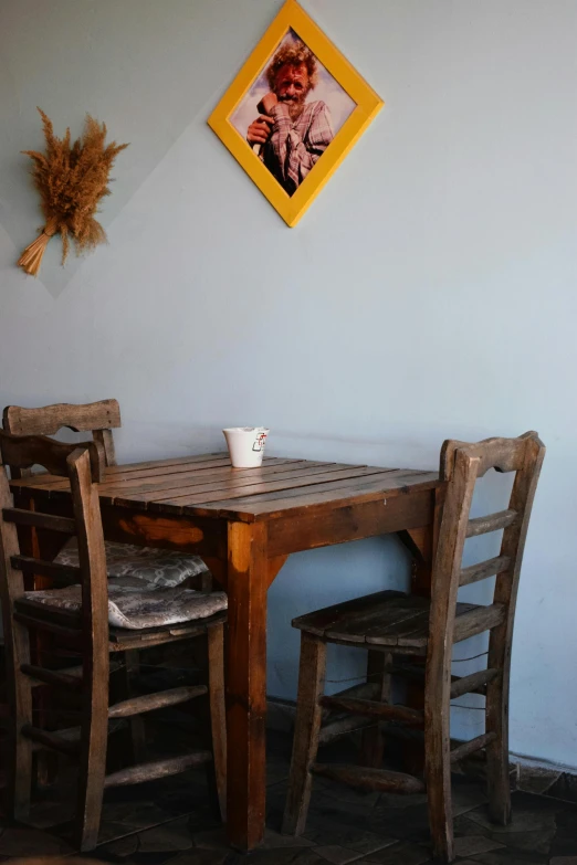 a wooden table topped with two chairs under a picture