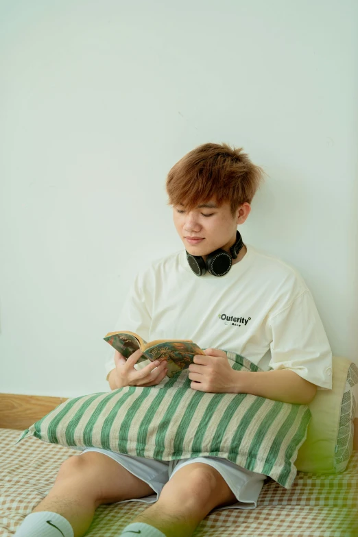 a young man reading a book on top of a bed