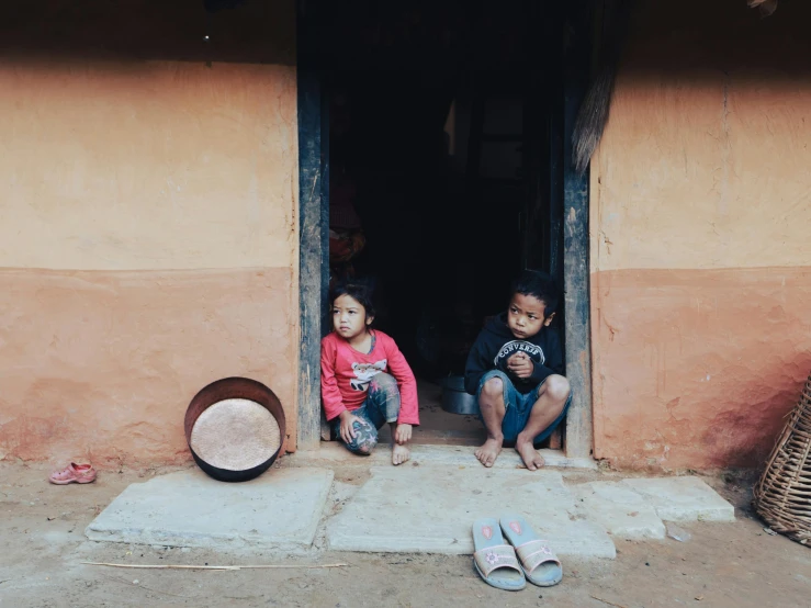 two children sitting in doorways on the ground