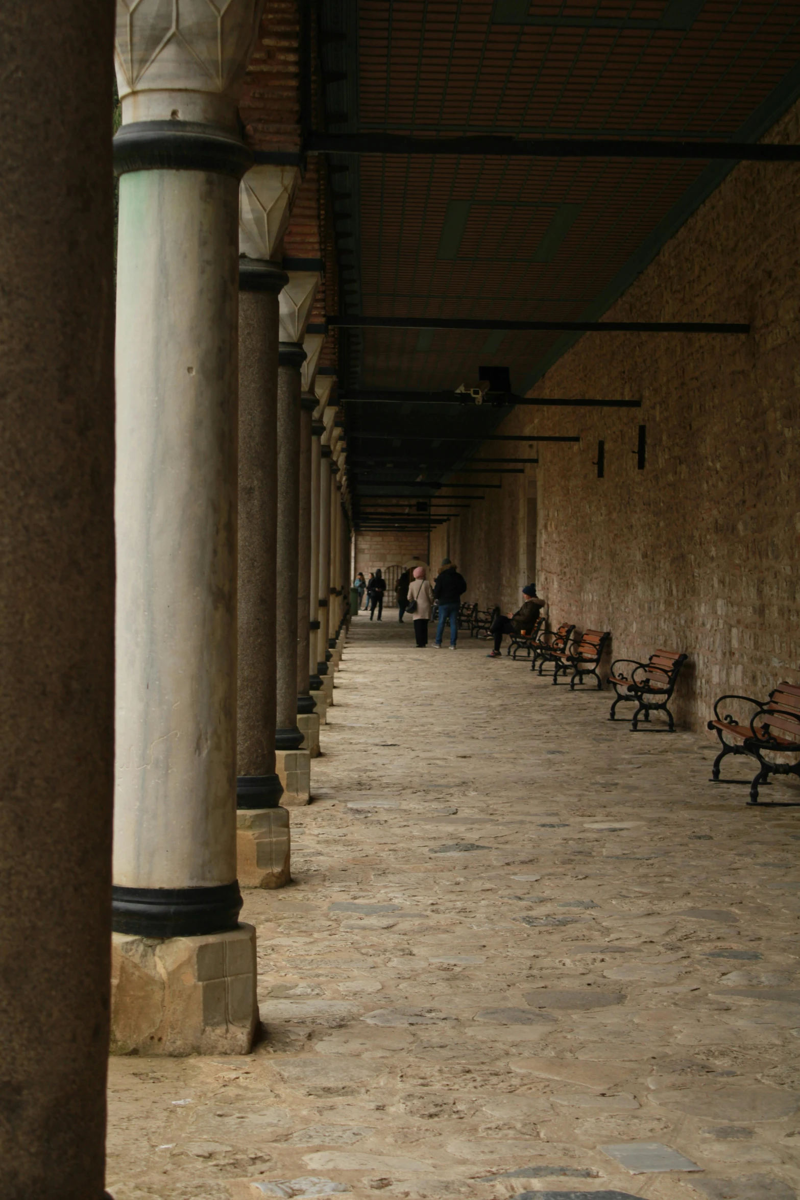 people walking on an enclosed walkway next to benches