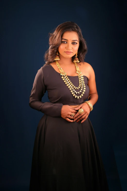 a woman in a dress with necklaces on, standing against a black background