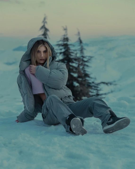 a young lady with winter clothing and boots sitting in the snow