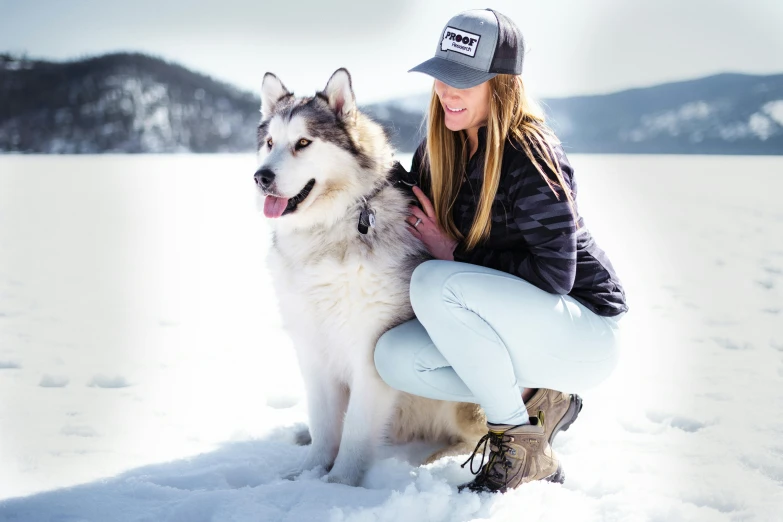 a beautiful woman sitting next to a husky dog on top of snow