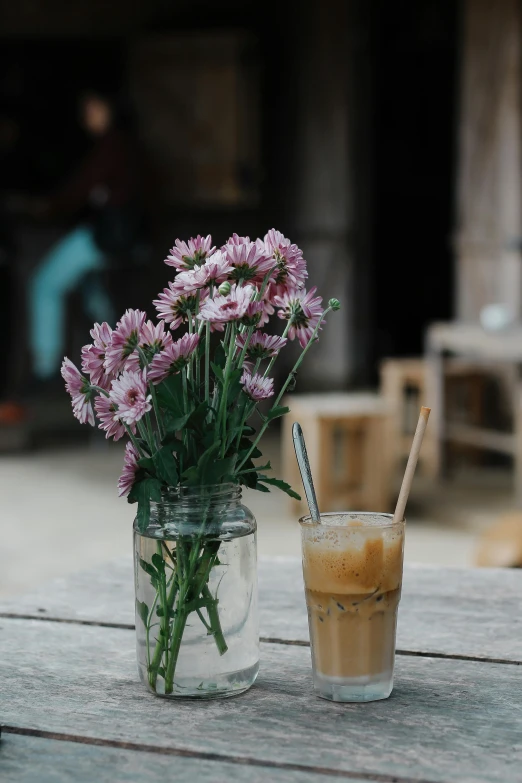 there is a glass with a drink and flowers in it