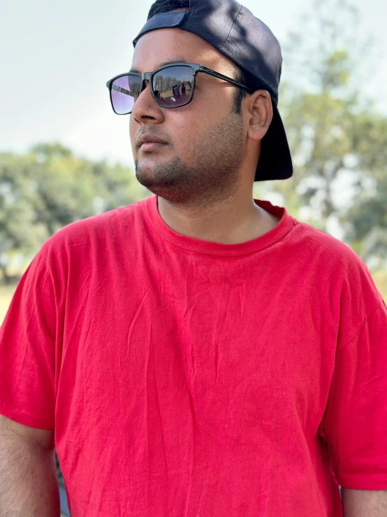 the man is wearing sunglasses, a hat and a red shirt