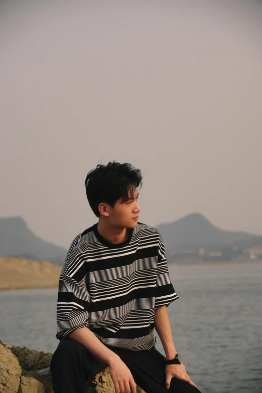 man in striped shirt sitting on rock near water