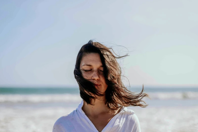 a woman at the beach looking down with hair blowing in the wind