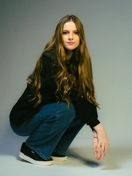 a girl with long hair kneeling and wearing jeans