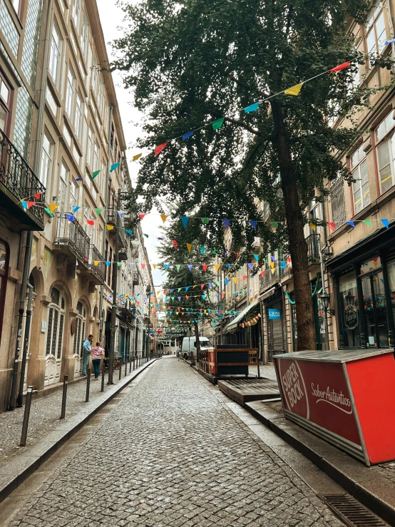 an empty street with trees and flags strung above